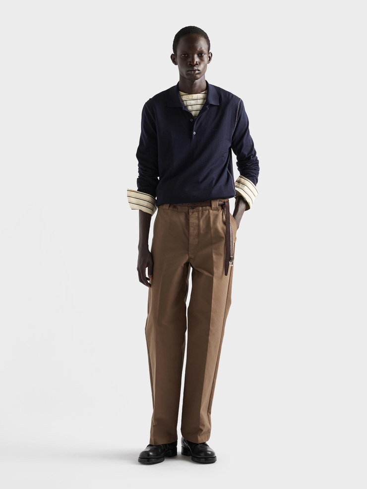 Input: brown pleated trousers worn under a layered knit and a shirt, with a bag strap in frame
