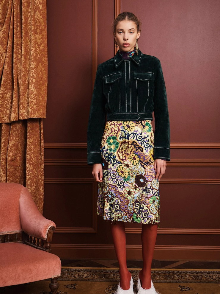 Input: an embellished skirt styled with a velvet jacket and red tights in a paneled room