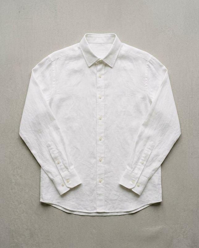Flat lay of a white long-sleeve linen shirt with a pointed collar and buttoned cuffs, on a pale gray surface