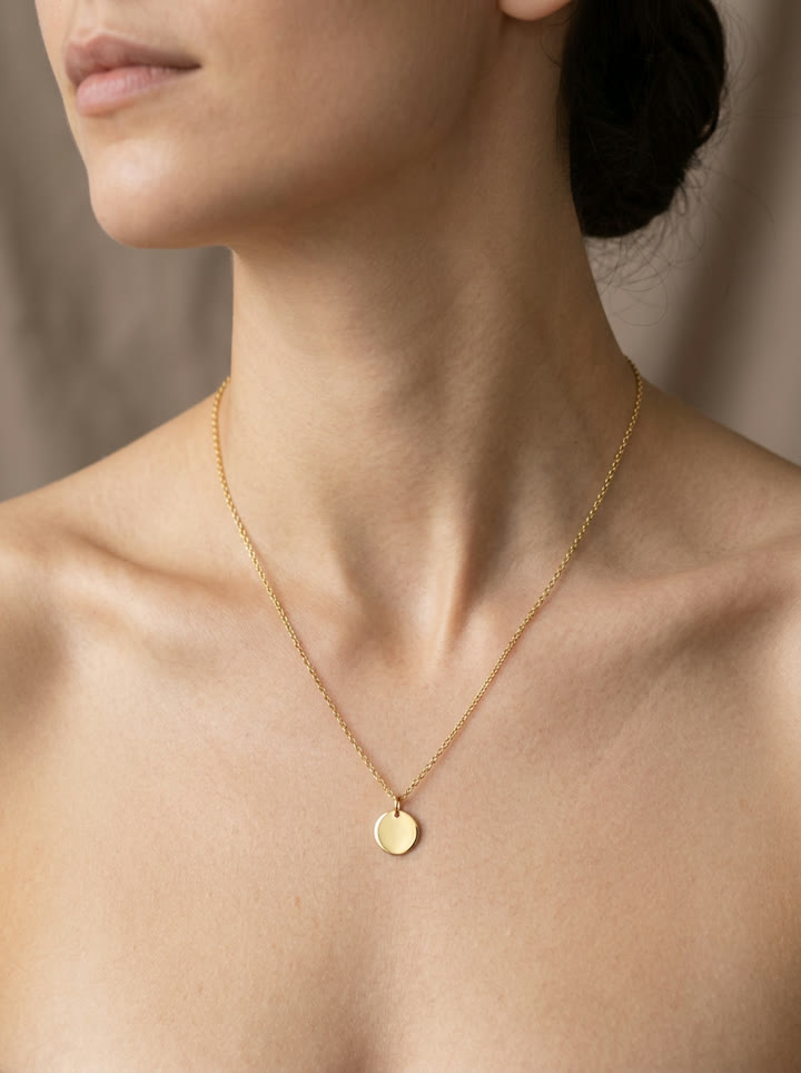 A fine gold cable chain with a small disc pendant on bare collarbone, the reference image